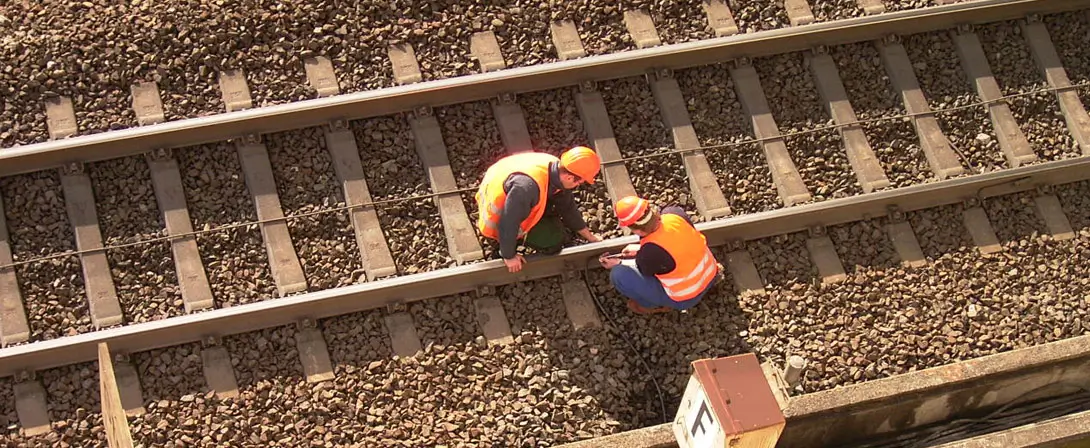 An einem Bahngleis arbeiten zwei Personen. Die Aufnahme ist aus der Vogelperspektive zu sehen.