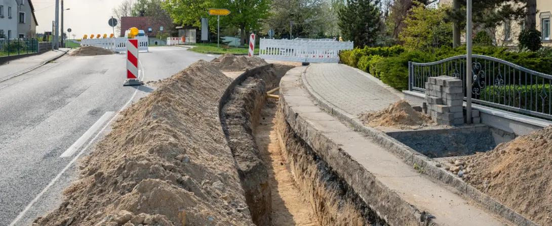 Am Straßenrand einer kleinen Straße wurde ein Graben für die Verlegung von Kabeln ausgehoben.