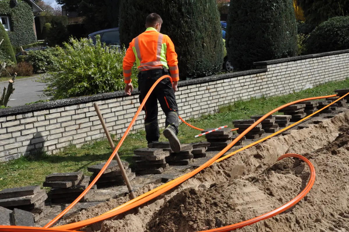 Ein Straßenbauarbeiter verlegt Kabel in einem speziell dafür ausgehobenen Graben.