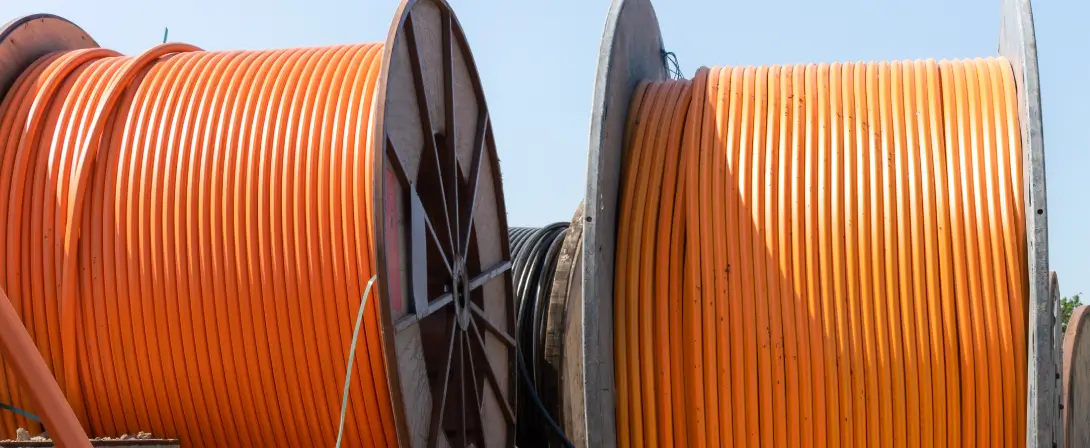 Zwei Kabeltrommeln mit orange ummantelten Kabeln befinden sich an einer Baustelle.